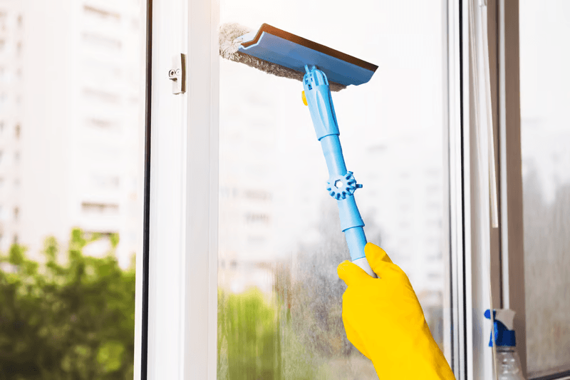A cleaner using a squeegee to wipe a home window streak-free